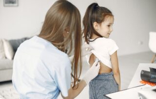A female family doctor examines a child with a stethoscope in a medical exam room during a well-visit checkup.