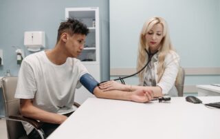 A doctor measures a male patient's blood pressure during a preventive care consultation in a clinic.