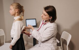 A doctor uses a stethoscope to examine a child during a sports physical in a clinic setting